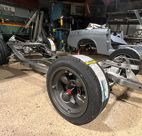 View of a car frame with wheels in a workshop setting.