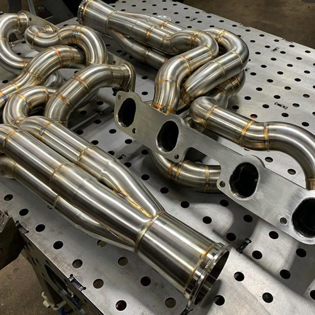 Stainless steel exhaust manifold on a perforated metal table.